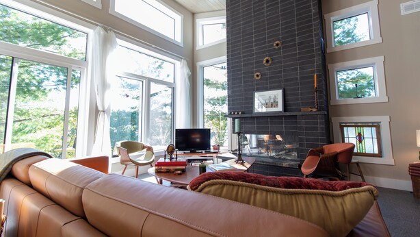 A modern living room with a fireplace, large windows, a sofa, and a television. - Luxury Lakefront Retreat | 3 bed,3 bath, near Parry Sound | Save on Weekly Stays (Parry Sound)