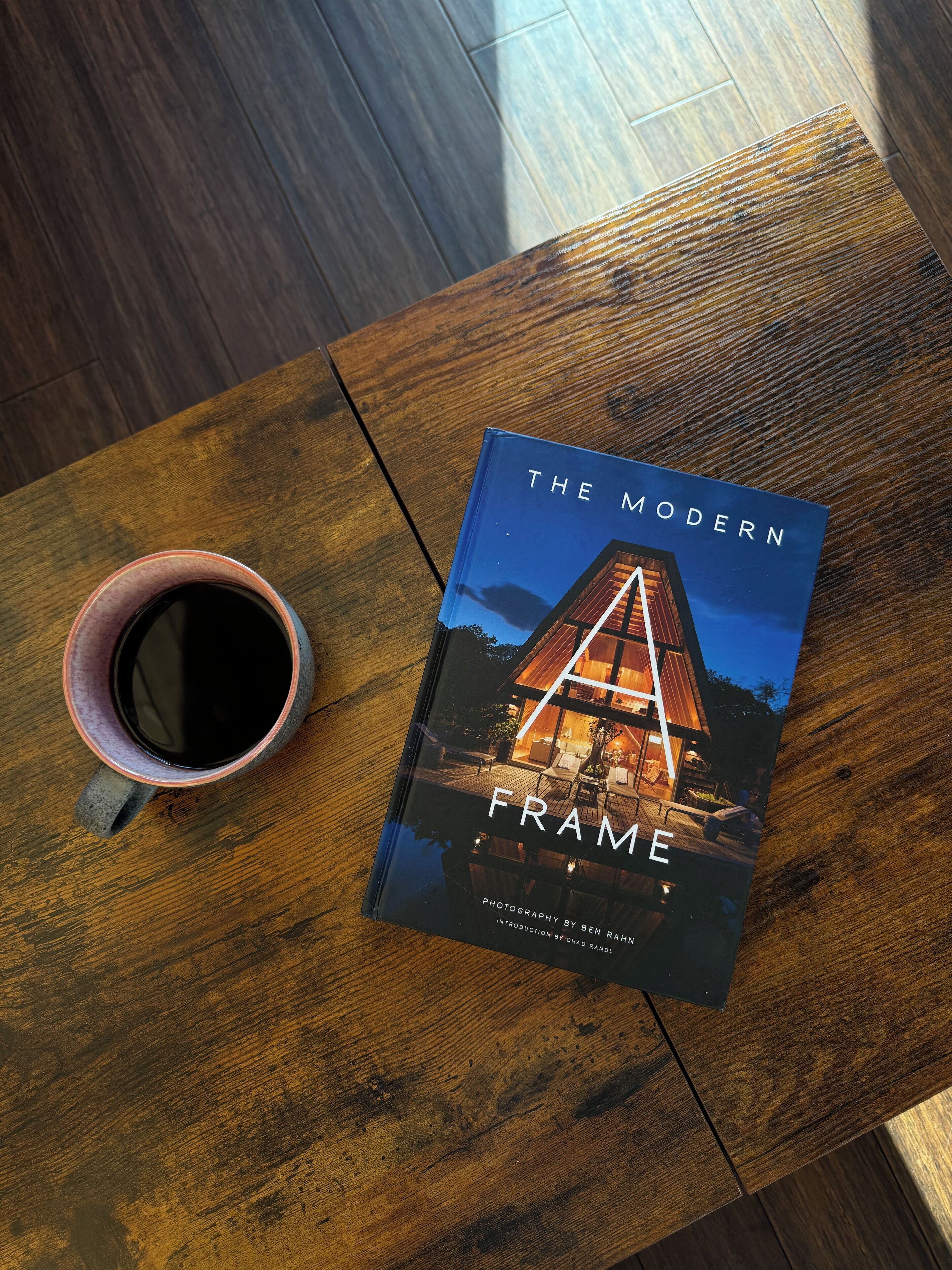 A book titled 'The Modern Frame' on a wooden table with a cup beside it.