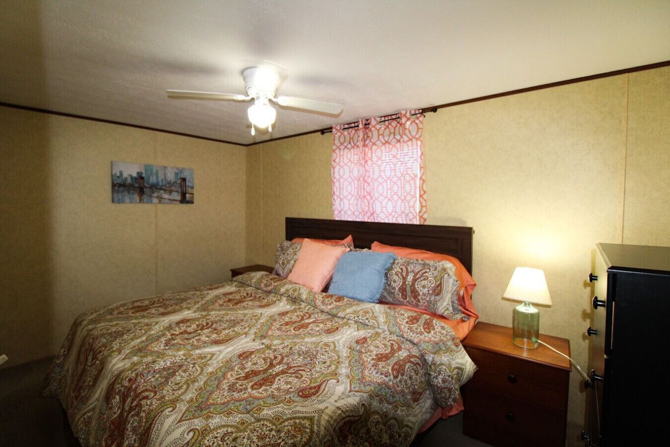 A bedroom with a bed, a nightstand, a lamp, a ceiling fan, and a wall-mounted TV.