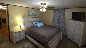 Un dormitorio con cama, mesitas de noche, televisor y ventilador de techo.