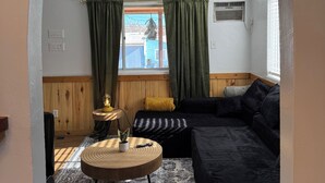 A cozy living room with a black sofa, a patterned rug, and a small wooden table with a lamp.