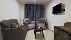 A living room with a sofa, two patterned armchairs, a coffee table, a TV mounted on the wall, and a dining table with chairs. - Masaya Aldiar (Amman)
