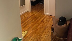 Una habitación con piso de madera, una cama al fondo y una puerta que da a otra estancia.