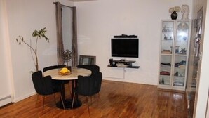 Un comedor con una mesa redonda, cuatro sillas, un televisor de pantalla plana montado en la pared y un armario con puertas de vidrio.