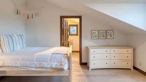 A bedroom with a bed, a dresser, and a door leading to another room.