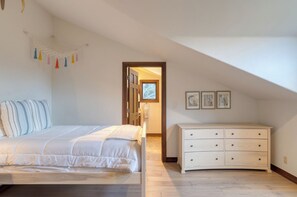 A bedroom with a bed, a dresser, and a door leading to another room.