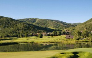 A golf course with a lake, surrounded by forested hills and residential buildings.