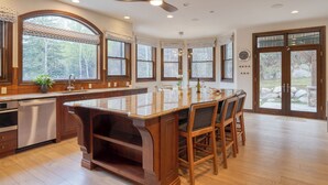 A spacious kitchen with a large island, wooden cabinetry, and a view of the outdoors through large windows.