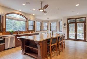 A spacious kitchen with a large island, wooden cabinetry, and a view of the outdoors through large windows.