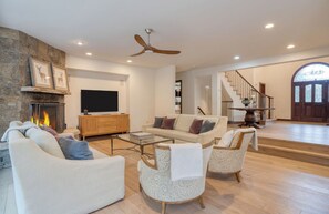 A spacious living room with a fireplace, a television, and a staircase leading to an upper level.