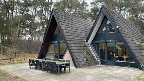 A modern, triangular-shaped building with a large patio area featuring a dining table and chairs. - Bungalow in Limburg Near Nature Reserves (Stramproy)