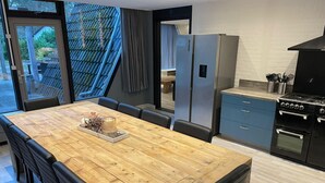 A modern kitchen with a wooden dining table, black chairs, a refrigerator, and a stove. - Bungalow in Limburg Near Nature Reserves (Stramproy)