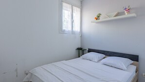 Makuuhuoneessa on sänky, yöpöytä, ikkuna, jossa on läpikuultavat verhot, sekä seinälle kiinnitetty hylly, jossa on koriste-esineitä.