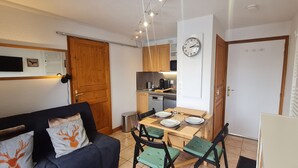 Un espacio habitable compacto con un sofá, una mesa de comedor para dos personas, una zona de cocina y un reloj de pared.