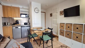 Una cocina compacta con microondas, estufa y refrigerador, un comedor con mesa y sillas, y un televisor montado en la pared.