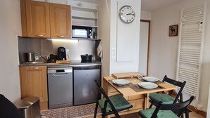 Cocina compacta con microondas, estufa y lavavajillas. Se observa una mesa de comedor con platos y vasos.
