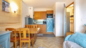 A compact kitchen with wooden cabinets, a refrigerator, and a dining area with a table and chairs. - Flat at the foot of the slopes with a balcony (Modane)