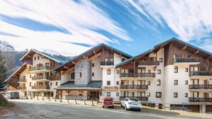 A multi-story hotel with balconies, a stone facade, and a mountain backdrop. - Flat at the foot of the slopes with a balcony (Modane)