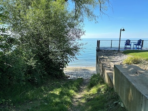 A pathway leading to a beach with a concrete barrier, a metal fence, and blue chairs.