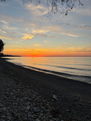 A pebbled beach with a sunset over the water.