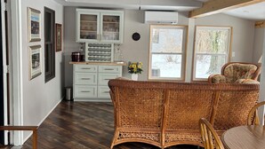 Una habitación amplia con piso de madera en patrón de espiga, un sofá de mimbre, una mesa de comedor con sillas y un ventilador de techo.