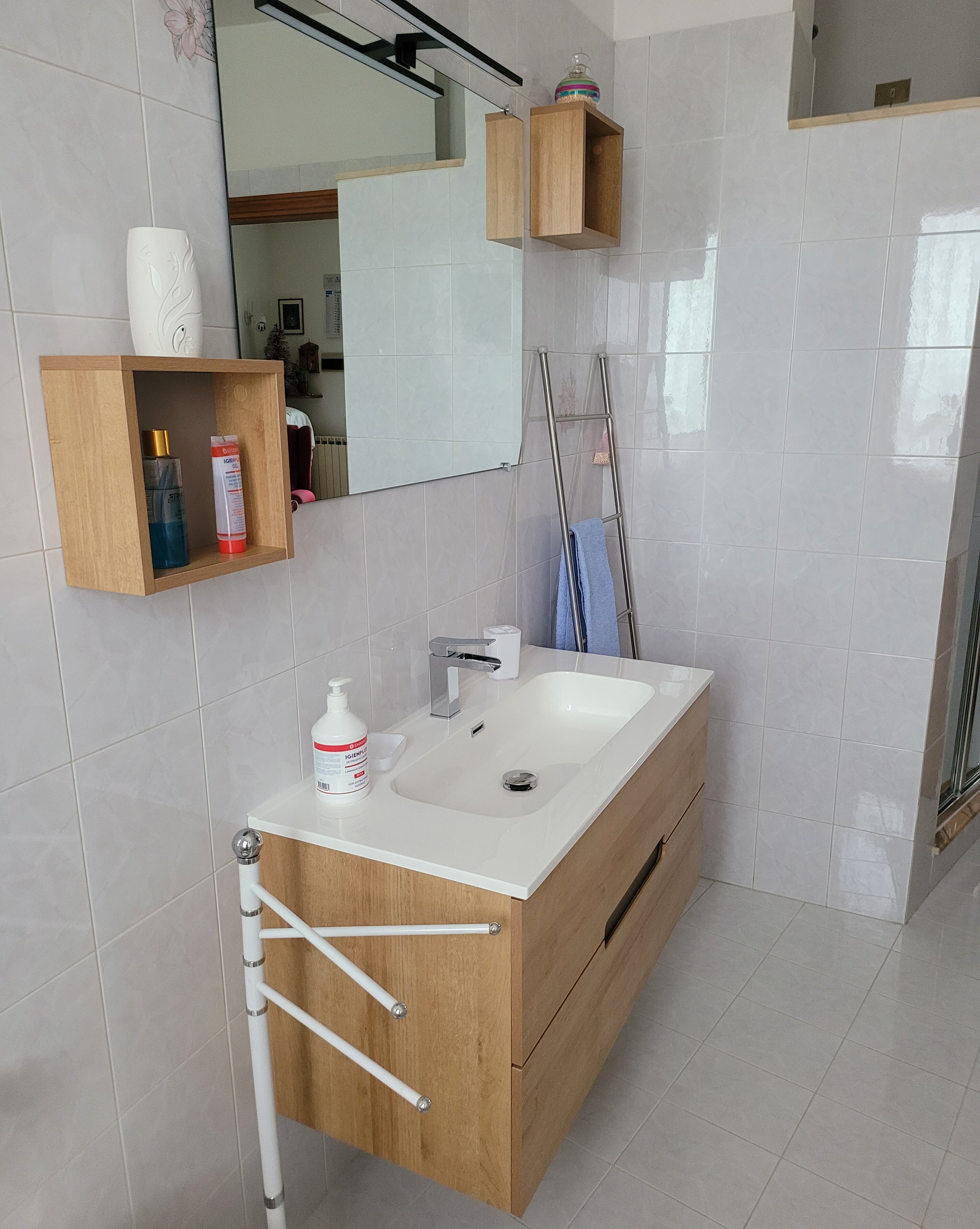 Une salle de bain moderne avec un meuble-lavabo en bois, un lavabo blanc et un miroir au-dessus. On y trouve des articles de toilette sur le meuble-lavabo et un porte-serviettes.
