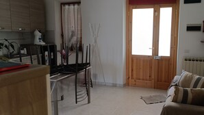 A living room with a sofa, a dining table with chairs, a kitchen area with cabinets, and a wooden door. - LANDLORD ALBACHIARA  (Ramazzano - Le Pulci)