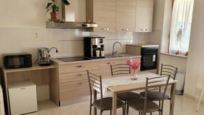 A modern kitchen with wooden cabinets, a built-in oven, a coffee machine, and a dining area with a table and chairs. - LANDLORD ALBACHIARA  (Ramazzano - Le Pulci)