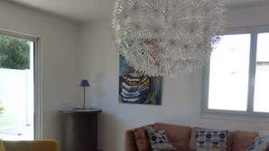 Un salon moderne avec un canapé, une table basse ronde et un fauteuil jaune. Une grande fenêtre laisse entrer la lumière naturelle et un tableau orne le mur.