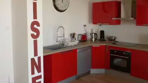 Une cuisine avec des armoires rouges, un évier, une horloge et un luminaire suspendu.