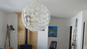 Un salon avec un canapé noir, un fauteuil jaune, une table basse ronde en bois, une cheminée noire et un lustre blanc.