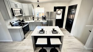 A modern kitchen with grey cabinets, stainless steel appliances, a central island with seating, and a black-framed window.