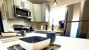 A modern kitchen with stainless steel appliances, a white countertop, and a bowl on a tray.