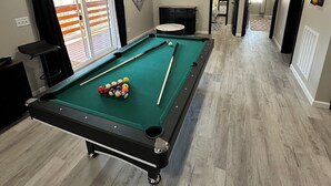 A pool table with balls, a ceiling fan, and a door leading to another room.