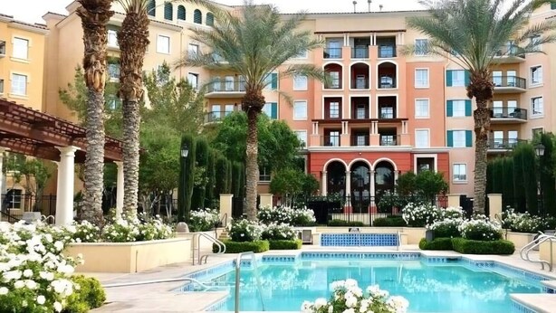 A hotel with a swimming pool surrounded by palm trees and white flowers, with a multi-story building in the background.