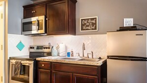 A kitchen with dark wood cabinets, a stainless steel oven, a microwave, a sink, and a refrigerator. There is a sign on the wall that says "Eat drink and be thankful."