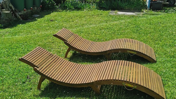 Dos sillones de madera en un patio césped con una valla de madera, un cobertizo pequeño y un árbol grande.