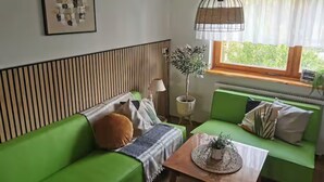 Un conjunto de sofá verde con una mesa de centro tejida, una lámpara de pie y un cuadro en la pared.