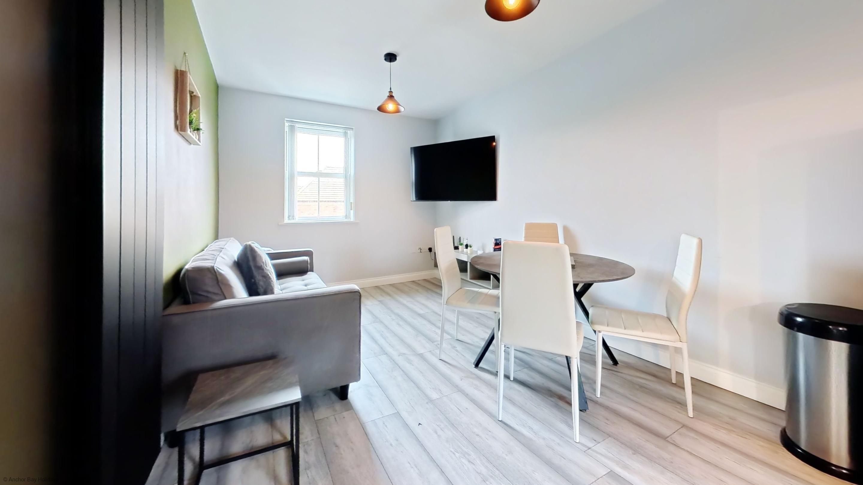 Ein modernes Wohnzimmer mit Sofa, Esstisch, Stühlen, Fernseher und Mülleimer.