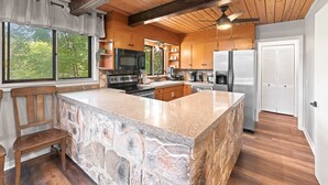 A kitchen with a large island, wooden cabinets, a stone countertop, and a ceiling fan. - Secluded Cabin for 10, Near Pkwy (Pigeon Forge)