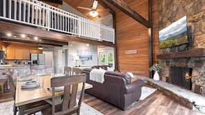 A spacious living area with a fireplace, a dining table set, a sofa, and a balcony. - Secluded Cabin for 10, Near Pkwy (Pigeon Forge)