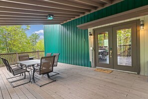 A covered outdoor seating area with a table and chairs, a door with glass panels, and a view of greenery. - Secluded Cabin for 10, Near Pkwy (Pigeon Forge)