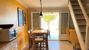 A dining area with a wooden table and chairs, a microwave on a cabinet, and a staircase leading to another level. - Vacation home 30 metres from the beach (Fleury)