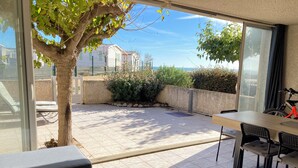 A patio with a table and chairs, a tree, and a view of buildings and greenery. - Vacation home 30 metres from the beach (Fleury)