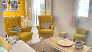 A living room with yellow armchairs, a wooden coffee table, and a sofa. There are framed pictures on the wall and a window with curtains. - Vacation home 30 metres from the beach (Fleury)