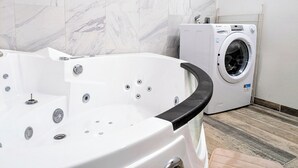 A bathroom with a marble-tiled wall, a white bathtub with black trim, and a front-loading washing machine. - Maison Auseths - Group accommodation - Campan (Campan)