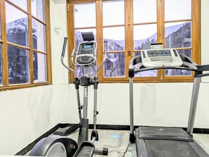 Un gimnasio con equipo cardiovascular, incluyendo una elíptica y una cinta de correr, y amplias ventanas con vistas a una montaña nevada.