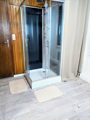 Un área de ducha con paredes de vidrio, una puerta de madera y un tapete beige en el suelo.