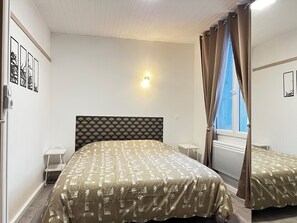 Una habitación de hotel con una cama, mesitas de noche, una lámpara de pared y una ventana con cortinas.