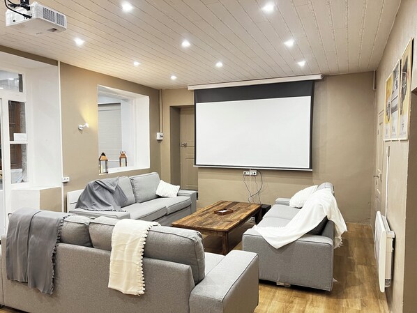 A modern living room with a grey sectional sofa, a wooden coffee table, and a large flat-screen TV mounted on the wall.